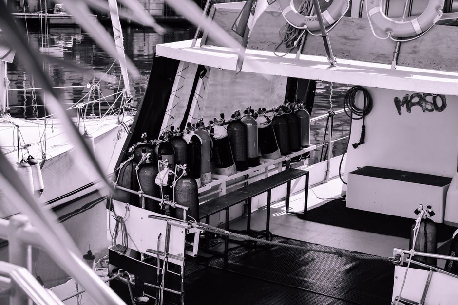 Black and white photo of a scuba diving boat with oxygen tanks at a harbor deck.
