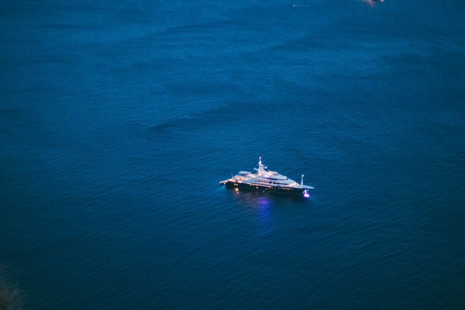Aerial view of a luxurious yacht illuminated at night on calm open waters.